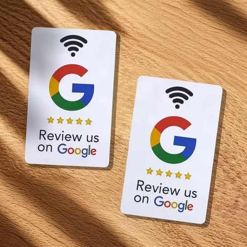 Two white Google review cards with the Google G logo and the text 'Review us on Google' are arranged on a wooden surface with white and yellow flowers around them.